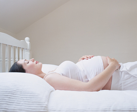 Young pregnant woman lying on bed, touching stomach, side view